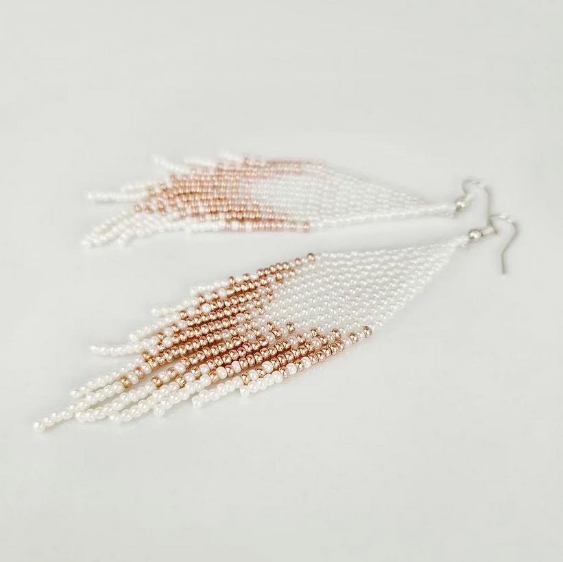 Two beaded tassels, one white and one rose gold, on a light gray background.