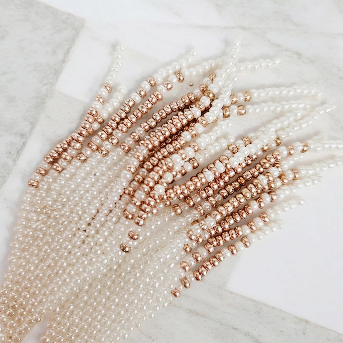 Close up of pearl and rose gold beaded strands on a marble surface