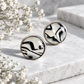Black and white zebra print round stud earrings with resin domes and stainless steel posts, displayed on white stone with delicate flowers.