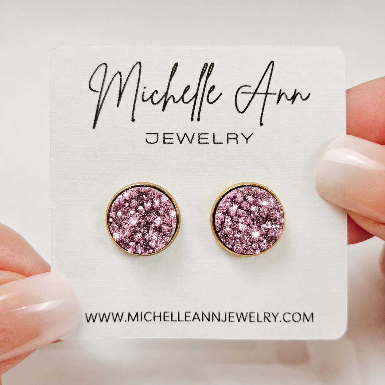 A pair of round 12mm purple faux druzy stud earrings with gold trim, displayed on a white Michelle Ann Jewelry card.
