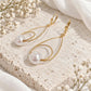 Gold teardrop pearl earrings displayed on pale ivory textured stone with white flowers and soft neutral fabric.