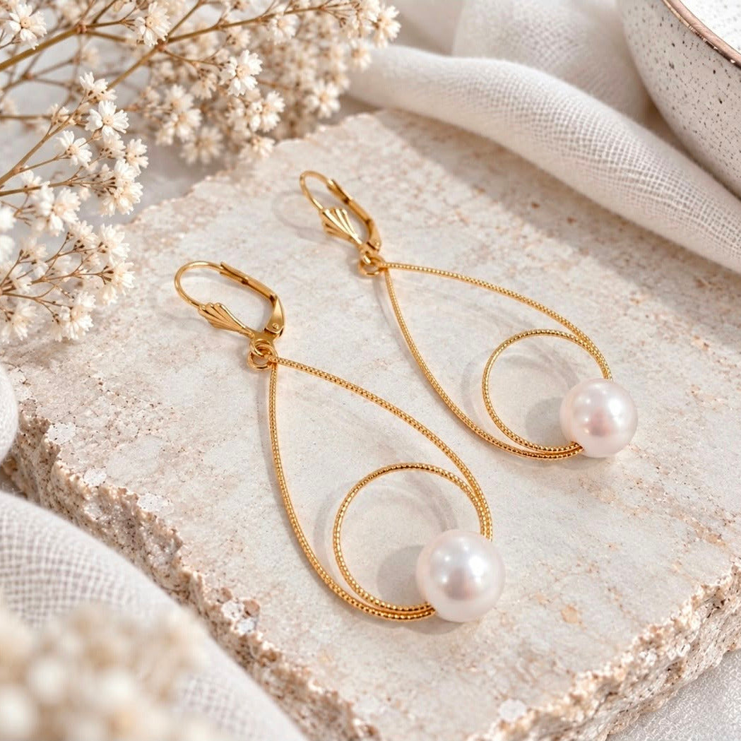 Gold pearl drop earrings styled on light cream stone with white baby’s breath and ivory fabric.