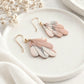 Blush pink, ivory and grey marbled polymer clay earrings with delicate gold accents arranged on a cream ceramic dish.