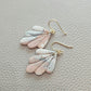 Close-up of handmade polymer clay fan earrings featuring soft pink, white and grey marbling, subtle metallic flecks and gold-tone hooks.