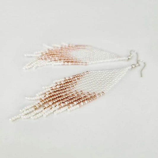 Two beaded tassels, one white and one rose gold, on a light gray background.