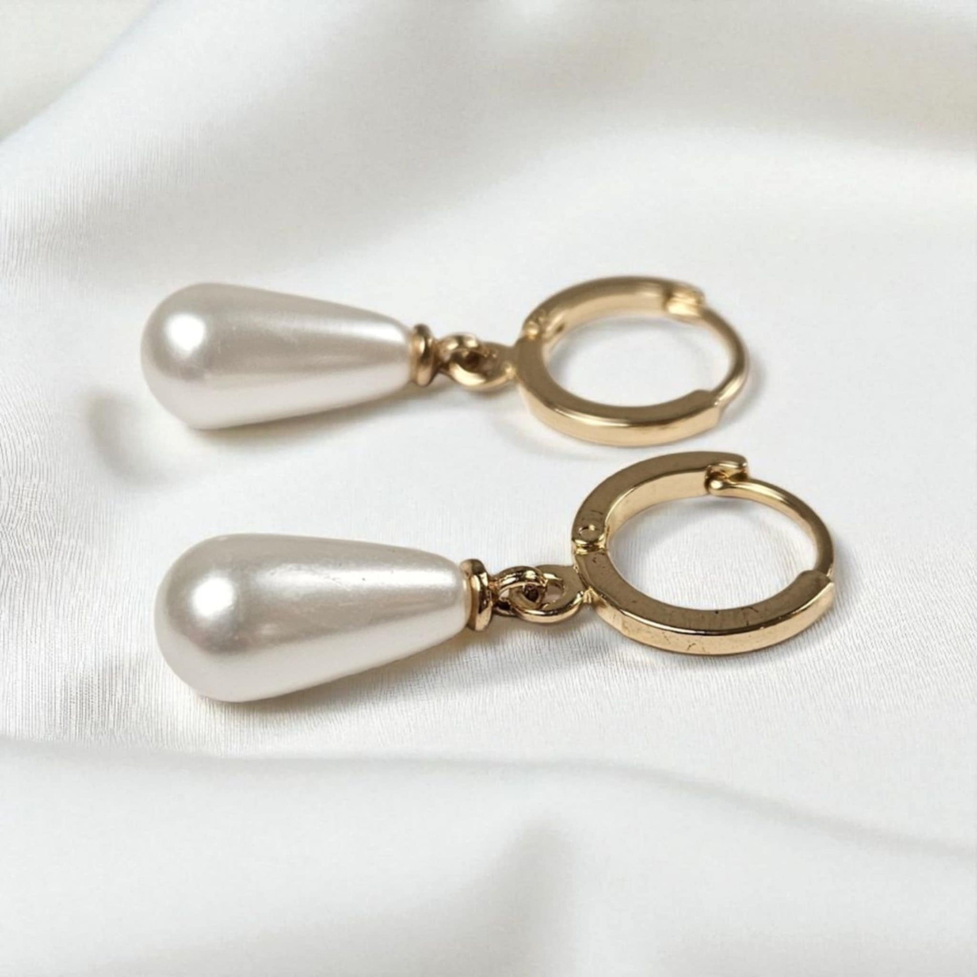 Pair of gold hoop earrings with pearl drops on a white background