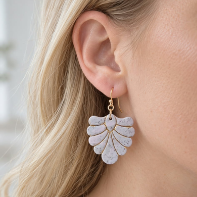Blush pink and ivory speckled polymer clay fan earrings with gold details worn on ear.