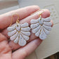 Hand holding blush pink and ivory speckled fan-shaped polymer clay earrings with gold hooks and gold detailing.