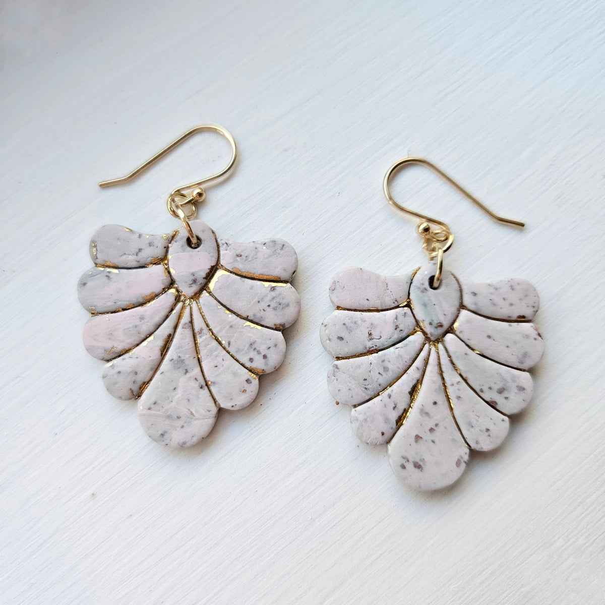 Blush pink and ivory speckled polymer clay fan earrings with gold accents on a white background.