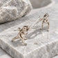 T-Rex dangle earrings with sterling silver ear wires displayed on grey stone.