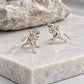 Silver T-Rex dinosaur earrings standing on a textured grey stone display.