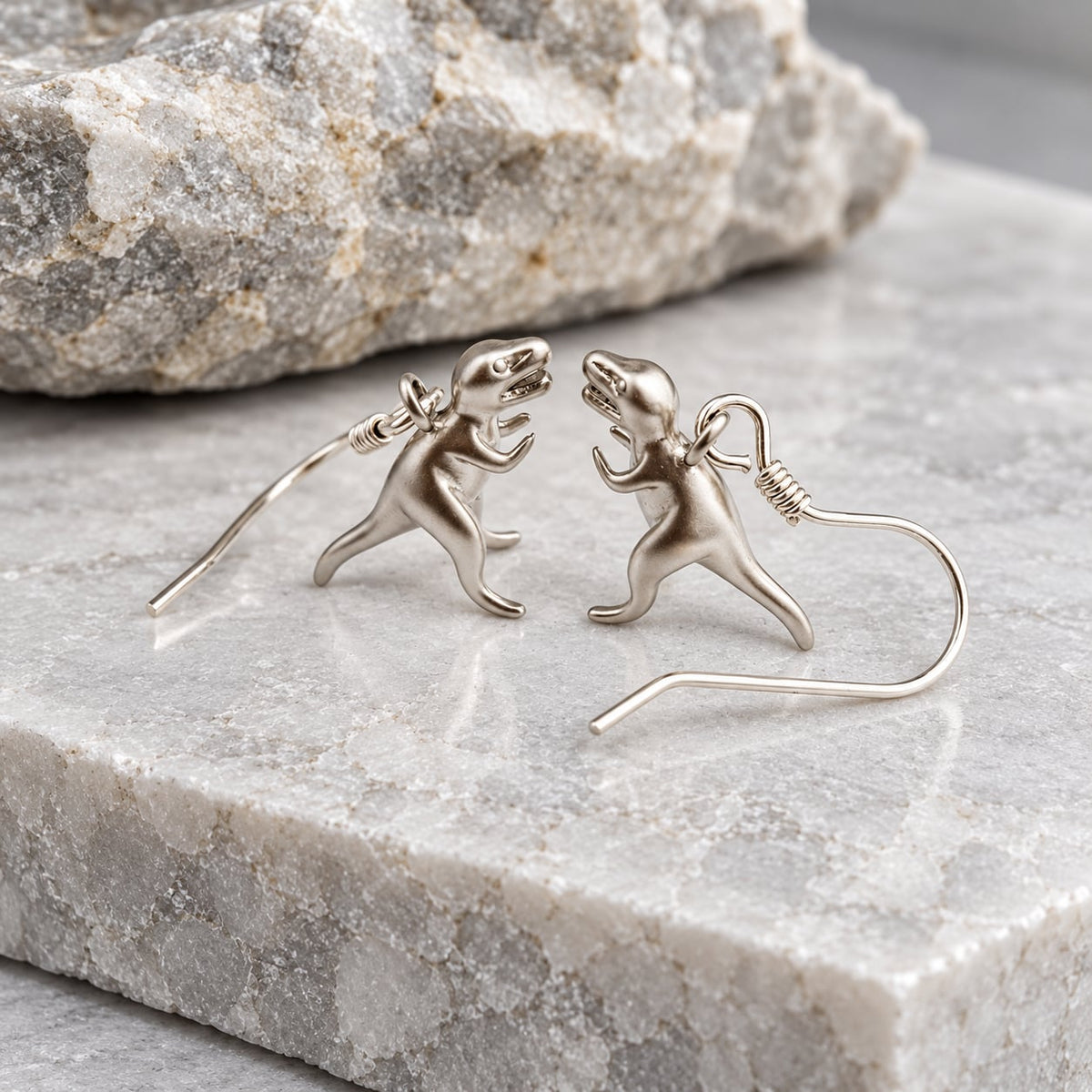 T-Rex earrings with sterling silver ear wires facing each other on textured stone.