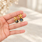 Hand holding a pair of gold floral earrings with smoky blue faceted teardrop stones against a soft neutral cream background.