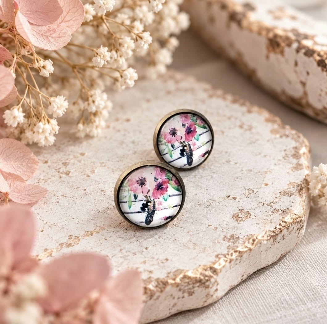 Pair of antique bronze floral stud earrings with pink, green and black wildflower artwork, styled with soft blush and white dried flowers.