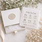 White Michelle Ann Jewelry gift box with cream botanical seal, polishing cloth and jewelry care card, styled with soft neutral flowers and ribbon.