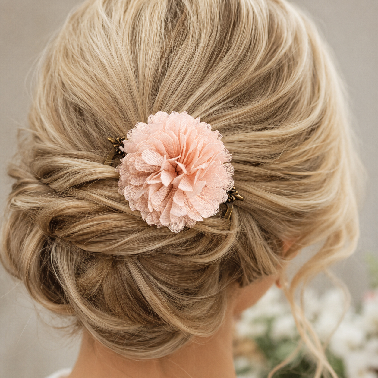 Elegant low bridal updo on a blonde model featuring an antique brass hair comb with a blush pink flower and decorative metal side details tucked into the hair.