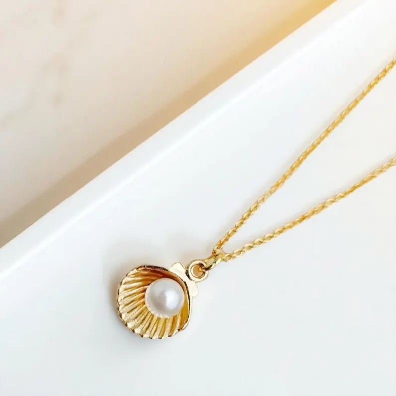 Gold seashell pendant necklace with pearl on gold chain. Photographed on a white subtle background.