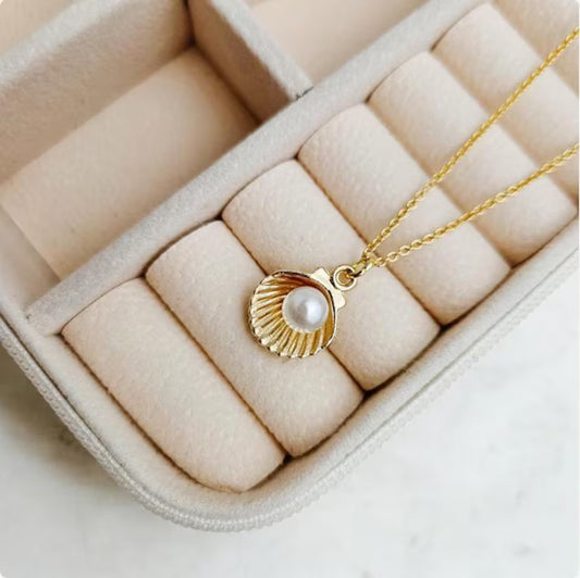 Gold seashell necklace with a white pearl pendant displayed in a soft neutral jewelry box.