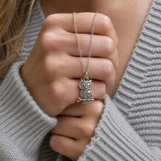 Silver owl pendant necklace held by a hand against a gray sweater background