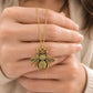 Gold bumblebee necklace pendant held up by hand in a centered shot, with a soft white outfit and warm natural lighting.